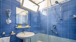 Une salle de bain avec des carreaux bleus, un lavabo blanc, un sèche-cheveux, une douche et un miroir.