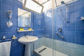 Une salle de bain avec des carreaux bleus, un lavabo blanc, un sèche-cheveux, une douche et un miroir.