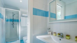 Une salle de bain avec une douche à parois de verre, un lavabo blanc avec des articles de toilette et un miroir au-dessus du lavabo.