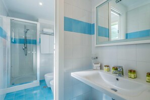 Une salle de bain avec une douche à parois de verre, un lavabo blanc avec des articles de toilette et un miroir au-dessus du lavabo.