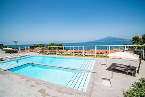 A swimming pool with clear blue water, surrounded by lounge chairs and umbrellas, with a view of the sea and a mountain in the background. - Hotel Le Axidie, BW Signature Collection (Vico Equense)