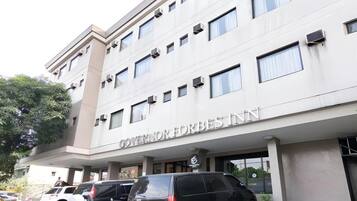 A multi-story building with the sign 'GOVERNOR FORBES INN' indicating a hotel. There are several parked vehicles in front, and the building has a modern architectural style with a flat roof and rectangular windows.