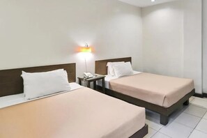 Quarto de hotel com duas camas, uma mesa de cabeceira com telefone e uma luminária na parede.