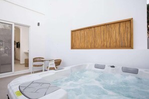 Un bain à remous avec un mur en panneaux de bois, une porte en verre et une petite table avec des chaises.