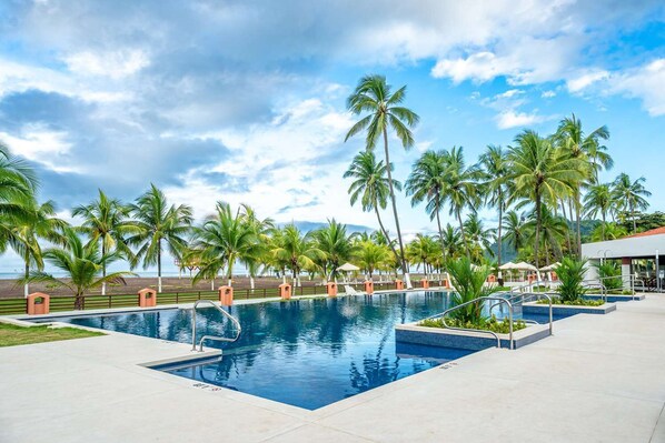 A swimming pool with palm trees, a clear sky, and a view of the beach. - Best Western Jaco Beach All Inclusive Resort (Jacó)