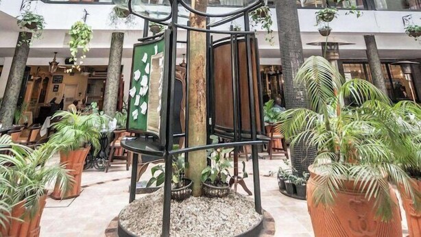 A spacious atrium with a central tree, multiple levels of seating, and potted plants. - Sarova Stanley (Nairobi)