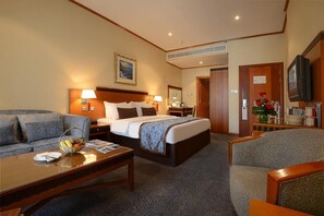 A hotel room with a bed, a sofa, a coffee table, a TV, and a painting on the wall. - Orchid Hotel Al Barsha Formerly Golden Tulip Al Barsha (Dubai)