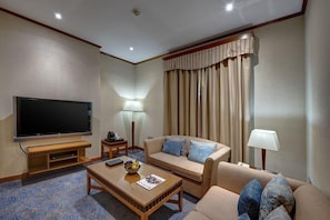 A hotel room with a flat-screen TV, a sofa, a coffee table, a lamp, and a large window with curtains. - Orchid Hotel Al Barsha Formerly Golden Tulip Al Barsha (Dubai)