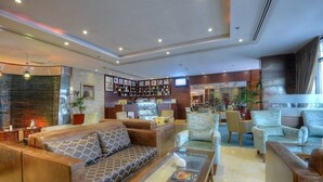 A modern lobby with leather sofas, a coffee table, and a bar area with various items. - Orchid Hotel Al Barsha Formerly Golden Tulip Al Barsha (Dubai)