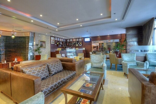 A modern lobby with leather sofas, a coffee table, and a bar area with various items. - Orchid Hotel Al Barsha Formerly Golden Tulip Al Barsha (Dubai)