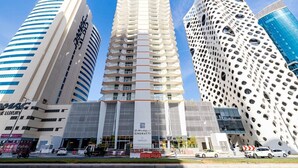 A modern building with a unique perforated facade, a central entrance with signage, and adjacent high-rise buildings. - Unlock Waterfront Edge Business bay (Dubai)