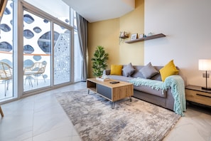 Un salon moderne avec un canapé, une table basse et une grande fenêtre donnant sur un immeuble doté de fenêtres rondes.