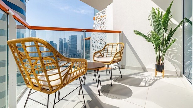 A balcony with wicker chairs, a small table, and a potted plant. - Unlock Waterfront Edge Business bay (Dubai)