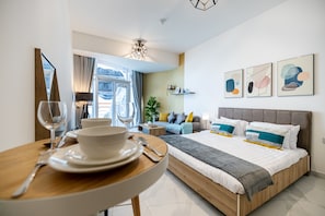 Una habitación de hotel moderna con cama, mesita de noche y un área de comedor con una mesa para dos.
