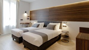 A modern bedroom with two beds, a wooden headboard, bedside lamps, and a small round table.
