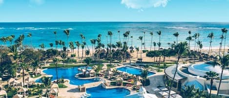 A resort with multiple swimming pools, palm trees, and a view of the ocean.
