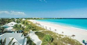 Un resort en la playa con una orilla de arena, palmeras y sombrillas.