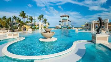 Piscina de resort con fuente central, palmeras y torre de salvavidas.