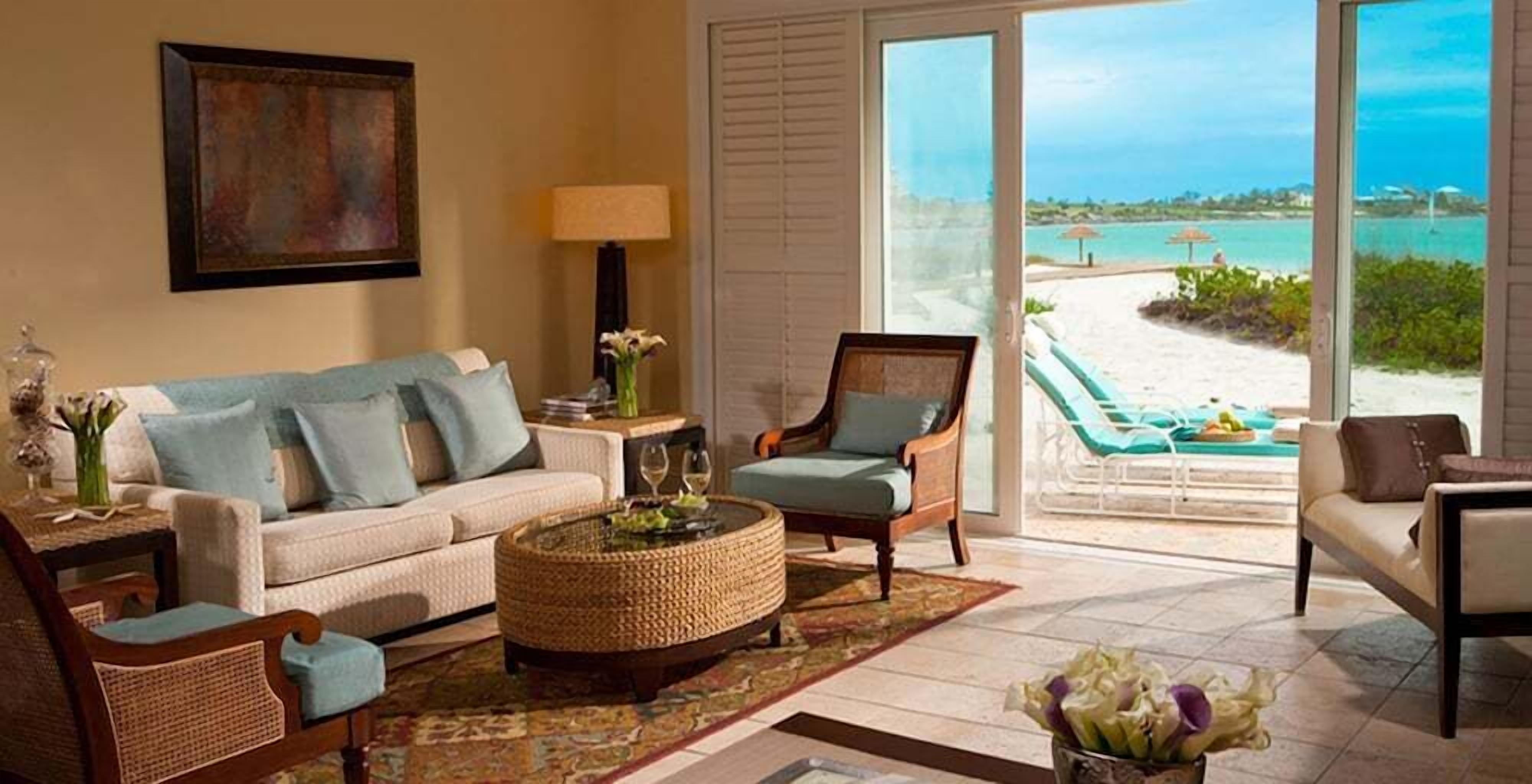 A living room with a sofa, armchairs, a coffee table, and a view of a beach through a sliding door.
