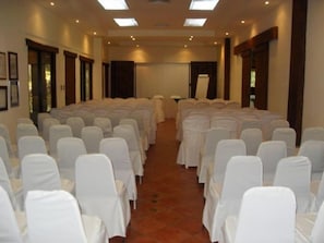 A conference room with rows of white chairs and tables, a large whiteboard, and a skylight ceiling. - Hacienda La Pacifica (Cañas)