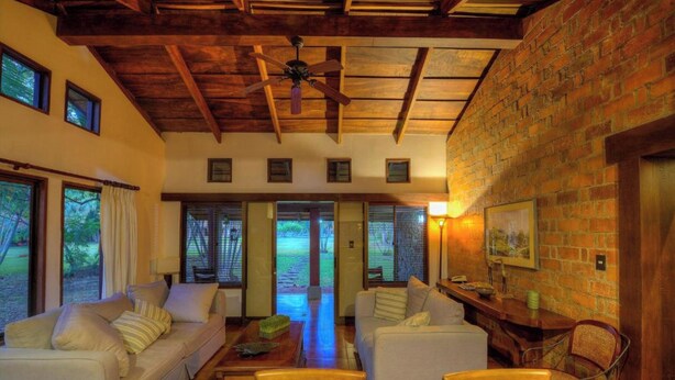 A cozy room with a wooden ceiling, a brick wall, and a large window. - Hacienda La Pacifica (Cañas)