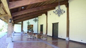 An outdoor covered patio with wooden beams, tiled flooring, and a dining area with chairs and a table. - Hacienda La Pacifica (Cañas)