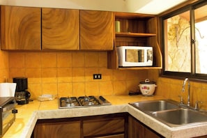 A kitchen with wooden cabinets, a microwave, a stove, and a sink. - Hacienda La Pacifica (Cañas)