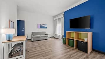 Un salon moderne comprenant un canapé, un téléviseur fixé au mur, une petite table avec une lampe et un coin cuisine.