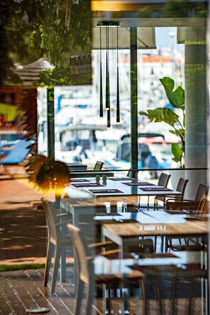 Un restaurante con terraza, grandes ventanales y lámparas colgantes.