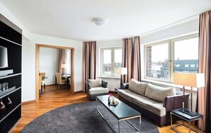 A modern hotel room with a sofa, armchairs, a coffee table, a TV, and a bookshelf. - Lindner Hotel Frankfurt Main Plaza, Part of Jdv by Hyatt (Frankfurt)