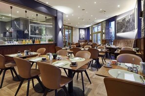 A restaurant with multiple tables and chairs, a bar area, and large windows. - Lindner Hotel Frankfurt Main Plaza, Part of Jdv by Hyatt (Frankfurt)