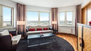 Un salon moderne comprenant un canapé, deux fauteuils, une table basse et une vue sur la ville grâce à de grandes fenêtres.