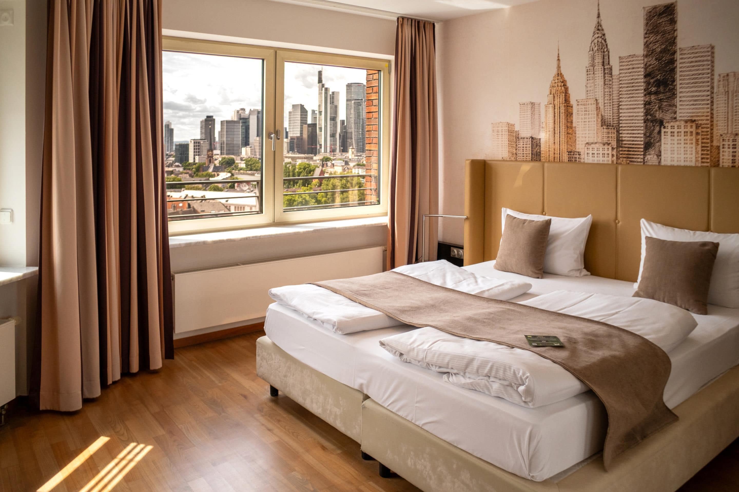 Habitación de hotel con una cama grande, vista panorámica de la ciudad y un cabecero con un mural urbano.