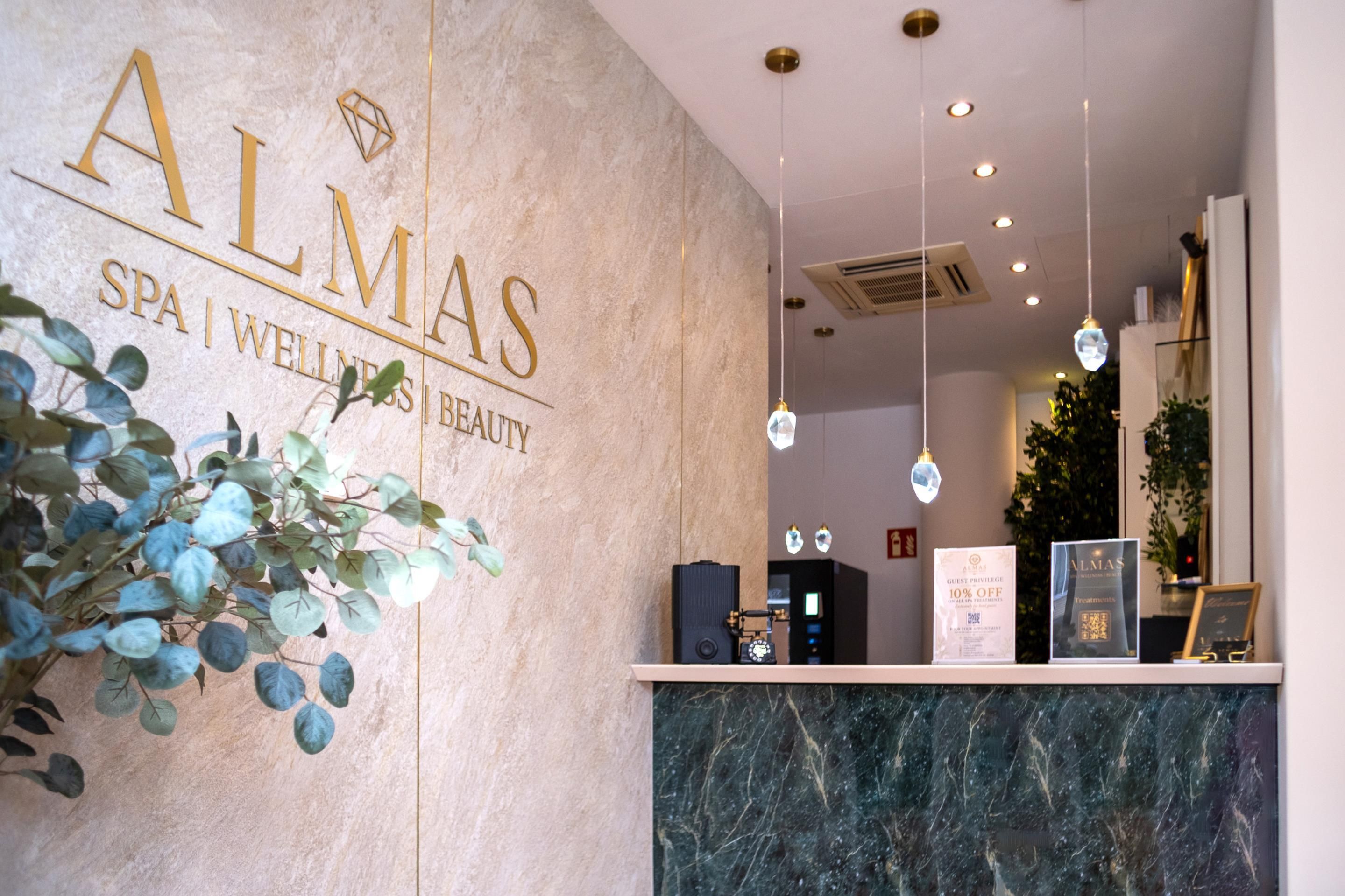 Un espace d'accueil avec un comptoir en marbre, une enseigne indiquant « ALMAS SPA | BIEN-ÊTRE | BEAUTÉ » et une plante placée à gauche.