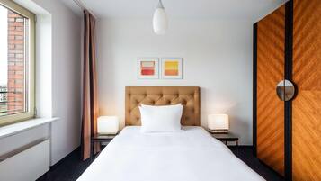 Ein Hotelzimmer mit einem großen Bett, zwei Nachttischlampen, einem Fenster mit Vorhängen und einer Wand mit Holzvertäfelung.