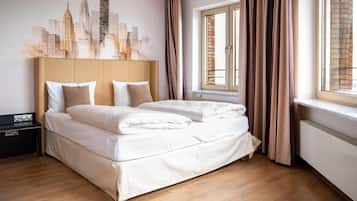 Habitación de hotel con cama, mesita de noche, ventana con cortinas y un mural de paisaje urbano en la pared.