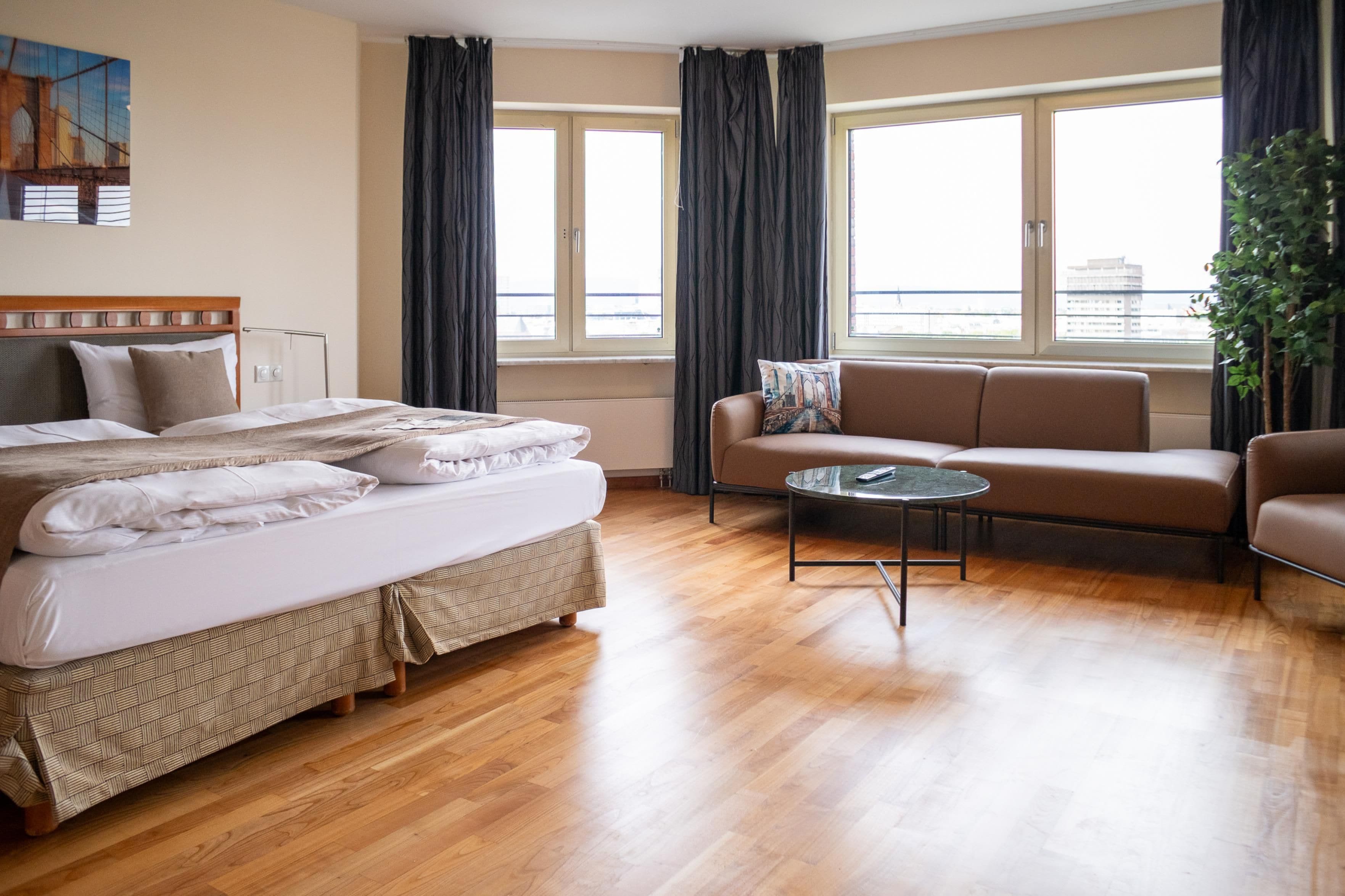 Una camera d'albergo con un letto, una poltrona, un tavolino e una finestra con tende.