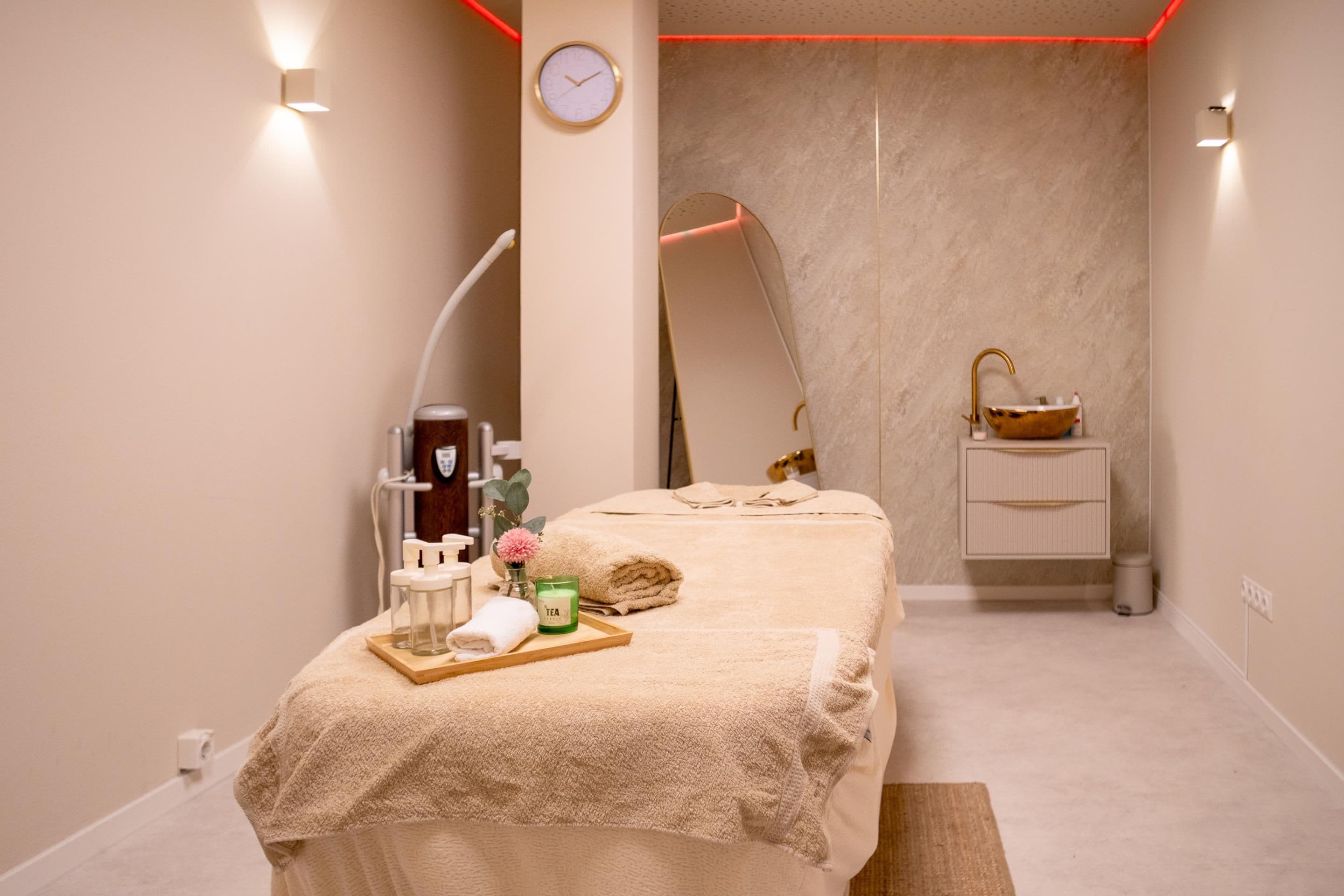 Un cuarto de spa con una cama, un lavamanos pequeño, una vela aromática y una botella de loción.