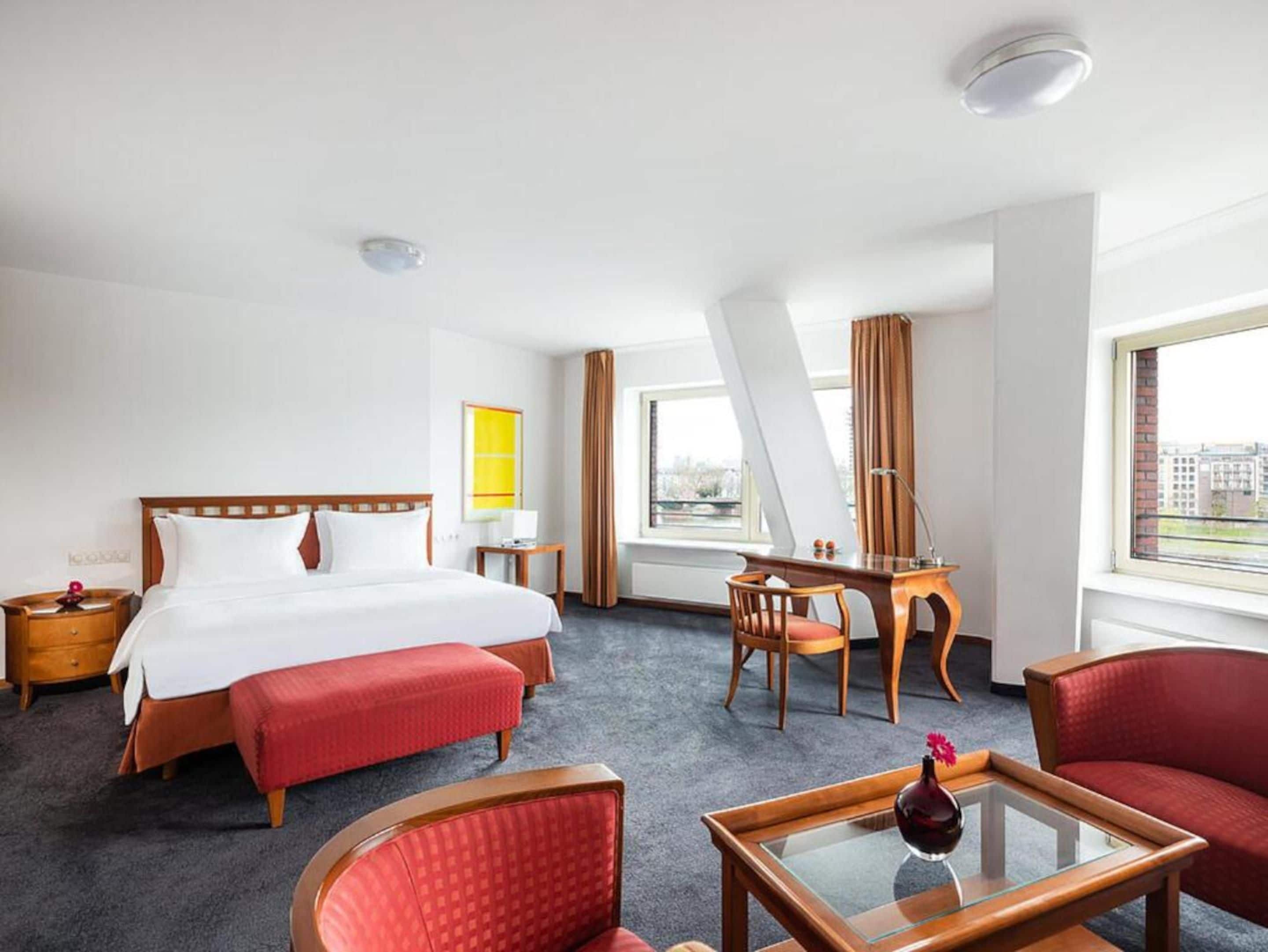 A hotel room with a bed, a desk, a chair, a sofa, and a view of the city.