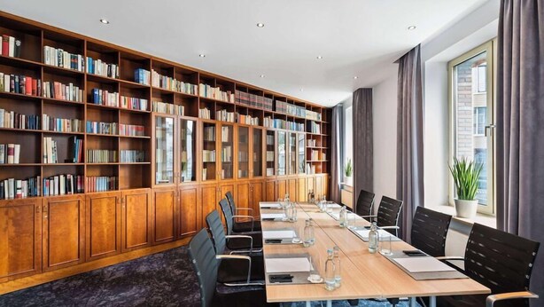 Une salle de conférence avec une longue table, des chaises et une bibliothèque remplie de livres.