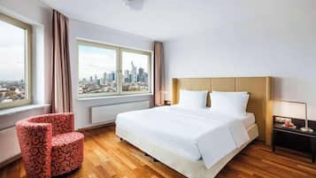 Ein Hotelzimmer mit einem großen Bett, einem Sessel, einem Nachttisch und einem Fenster mit Blick auf die Stadt.