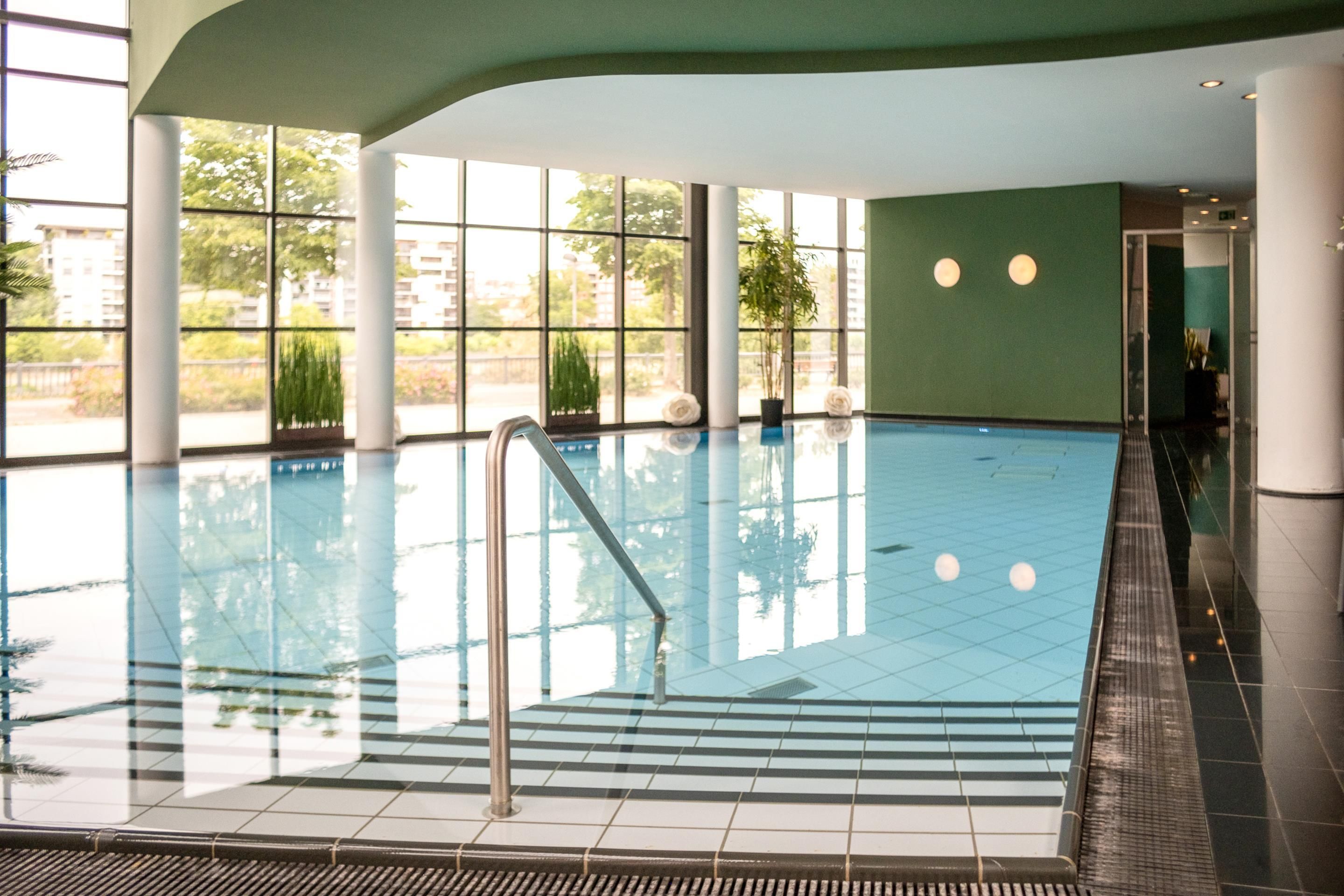 An indoor swimming pool with clear glass walls, a metal ladder, and a tiled floor.