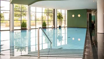 An indoor swimming pool with clear glass walls, a metal ladder, and a tiled floor.
