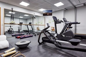 A gym with exercise equipment, a large mirror, and a view of the city. - Lindner Hotel Frankfurt Main Plaza, Part of Jdv by Hyatt (Frankfurt)