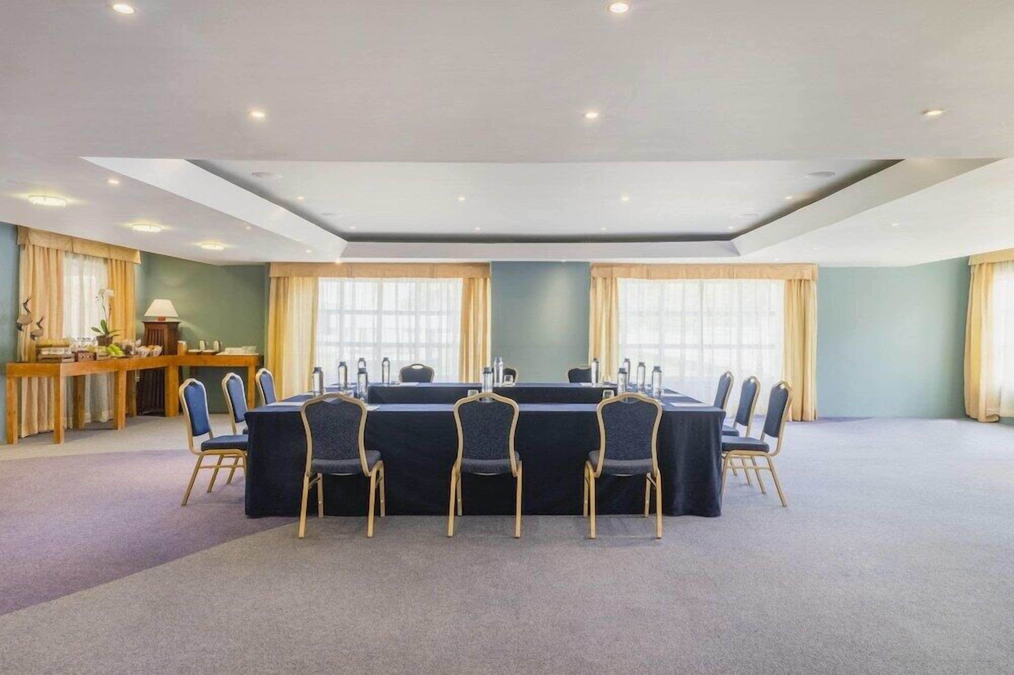 A conference room with a long table, chairs, a podium, and a desk with a lamp.