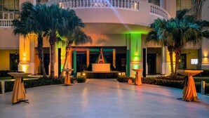 A hotel lobby with a central fountain, palm trees, and tables set up for events. - Iberostar Waves Rose Hall Beach All Inclusive (Montego Bay)