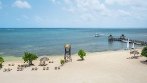 A beach with lounge chairs, a thatched hut, and a pier extending into the water. - Iberostar Waves Rose Hall Beach All Inclusive (Montego Bay)