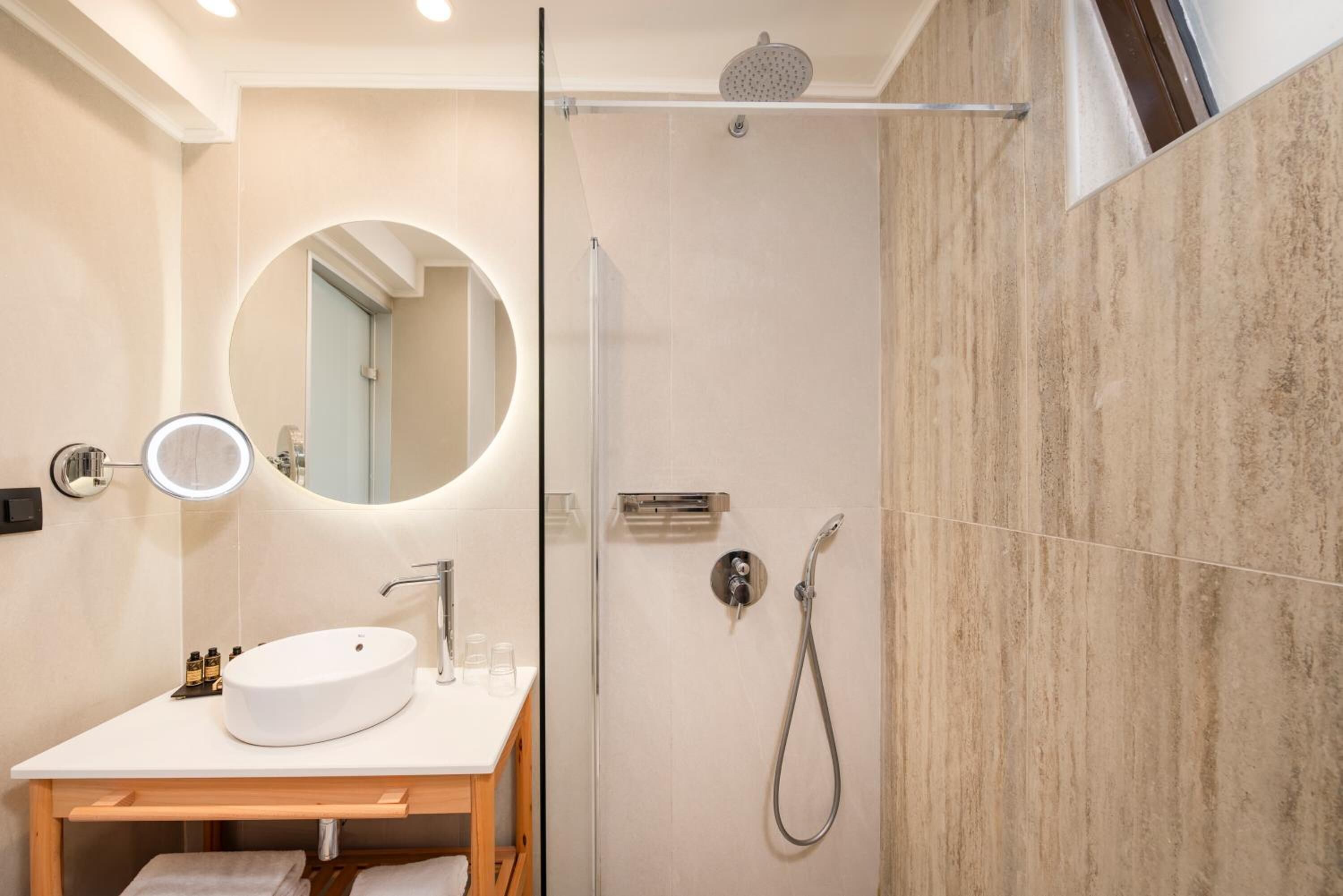 Un baño moderno con un espejo redondo, un lavabo, una ducha y cabina de ducha con paredes de vidrio.