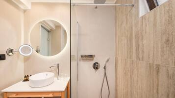 Un baño moderno con un espejo redondo, un lavabo, una ducha y cabina de ducha con paredes de vidrio.