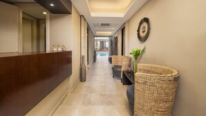 Uma área de recepção de hotel, com balcão, sala de espera com cadeiras, objeto decorativo na parede e uma cesta de vime grande.